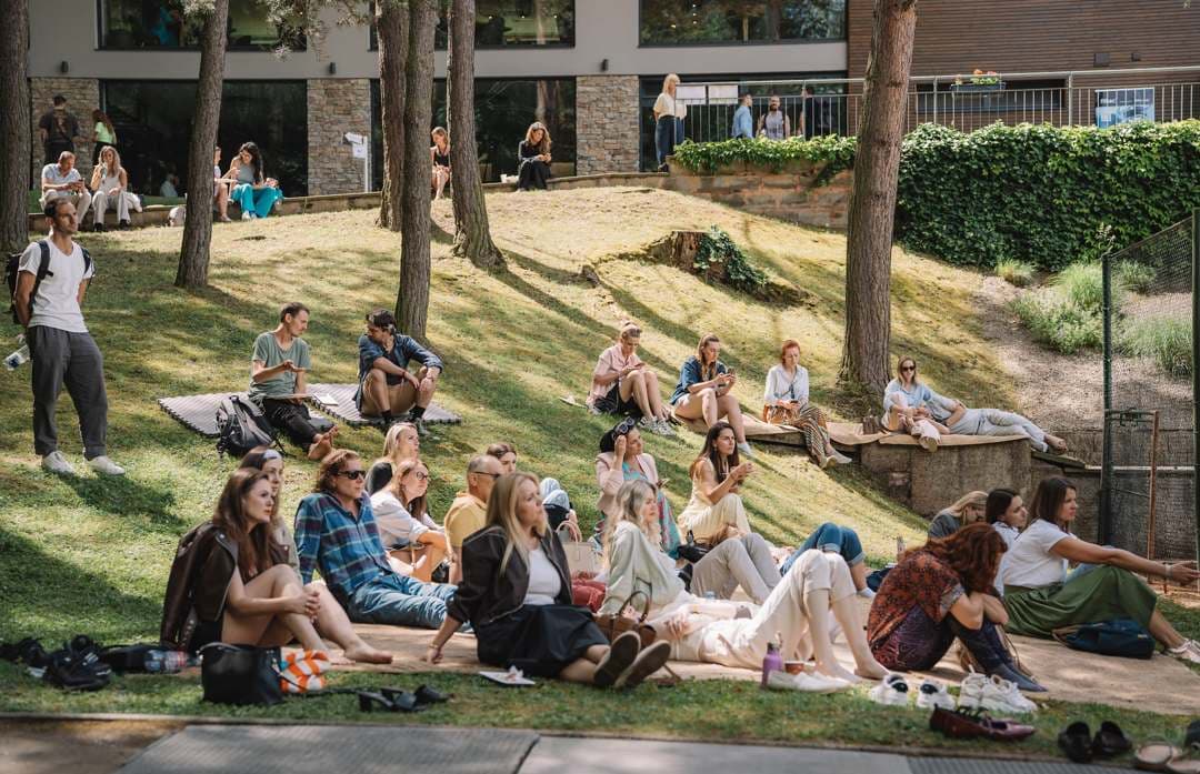 Lidé sedí na trávě ve svahu zahrady Vista Resortu mezi bloky programu